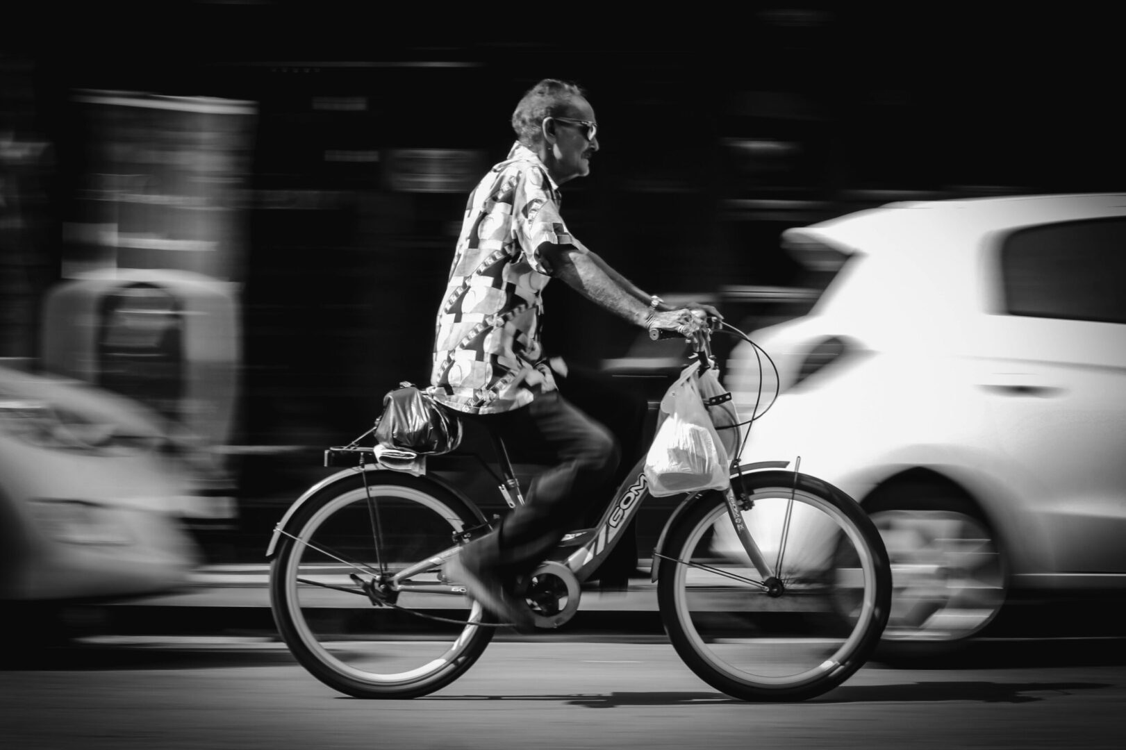 A man rides a bicycle fast through city streets. Urban life captured in motion.